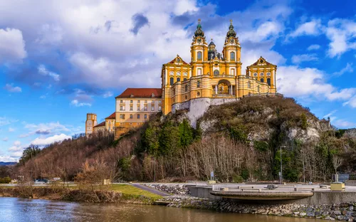 Barocke Abtei auf Hügel mit Fluss im Vordergrund und blauem Himmel im Hintergrund.