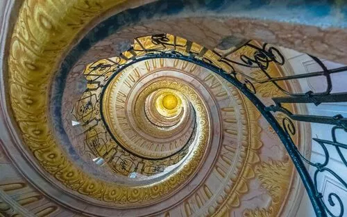 Blick nach oben in ein kunstvoll verziertes Wendeltreppenhaus mit geschmiedetem Geländer.