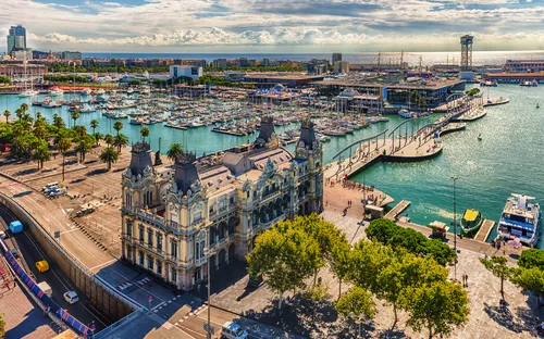 Hafen von Barcelona mit historischem Gebäude und Yachten im Wasser.