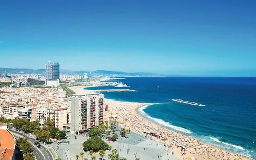Strand und Küstenlinie einer Stadt mit vielen Menschen und Gebäuden im Hintergrund.