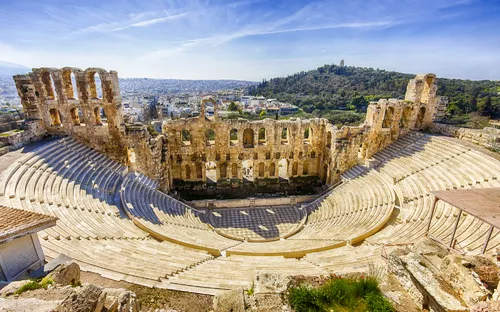Antikes Amphitheater in sonniger Landschaft vor bewaldetem Hügel.
