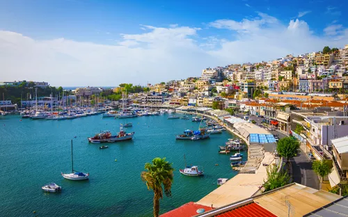 Hafen mit Segelbooten, umgeben von Gebäuden auf einem Hügel bei klarem Himmel.