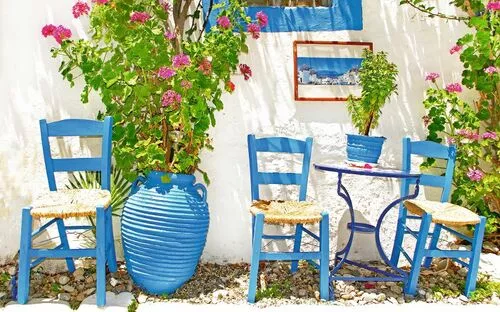 Drei blaue Stühle und ein Tisch in einem mediterranen Garten mit blühenden Pflanzen.