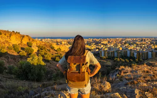 Frau mit Rucksack blickt von Hügel auf Stadt in der Abendsonne.
