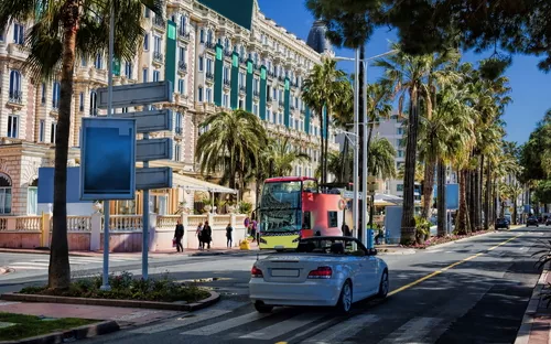 Straßenszene mit Palmen, vorbeifahrendem Bus und Cabrio in einer Stadt.