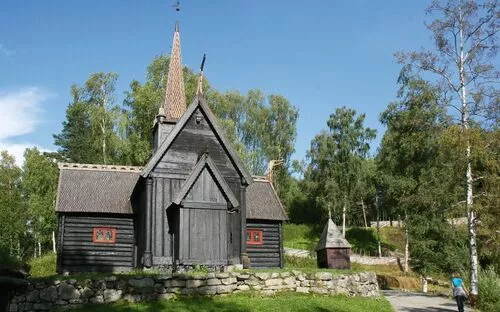 Holzkirche im Freilichtmuseum Maihaugen, umgeben von Bäumen und einem blauen Himmel.