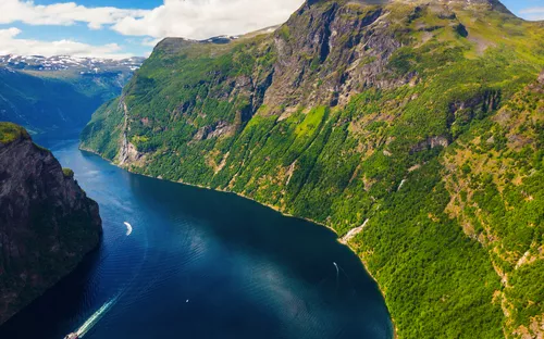 Norwegischer Fjord mit steilen, grünen Berghängen und einem Schiff auf dem Wasser.