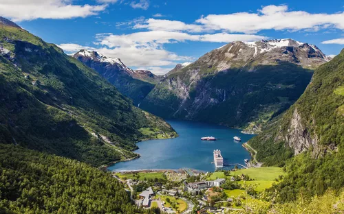 Blick auf den Geirangerfjord mit Bergen und einem Kreuzfahrtschiff im Wasser.