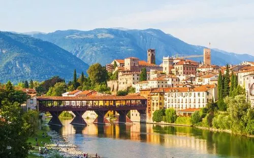 Mittelalterliche Stadt am Fluss mit Brücke und Bergen im Hintergrund