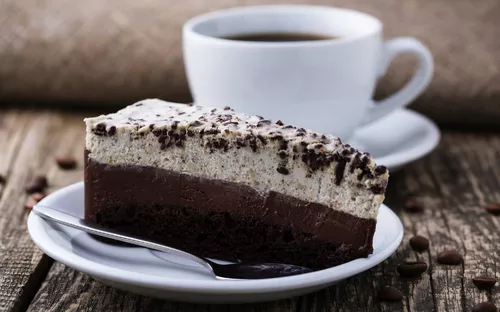 Ein Stück Schokoladenkuchen mit Sahne und Kaffeetasse im Hintergrund.