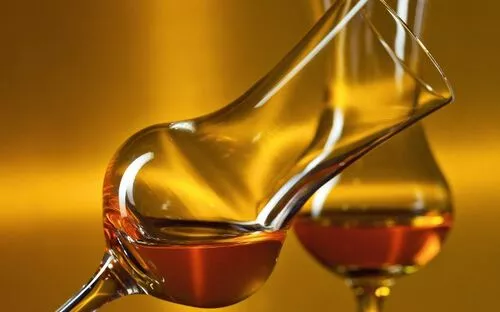 Zwei Cognacgläser mit brauner Flüssigkeit vor goldfarbenem Hintergrund.