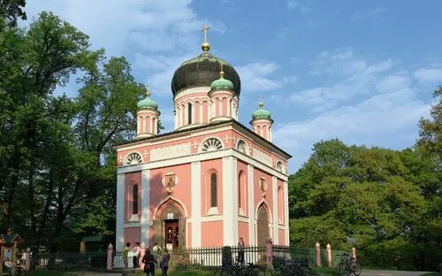 Rosa orthodoxe Kirche mit Zwiebeltürmen im Grünen unter blauem Himmel.