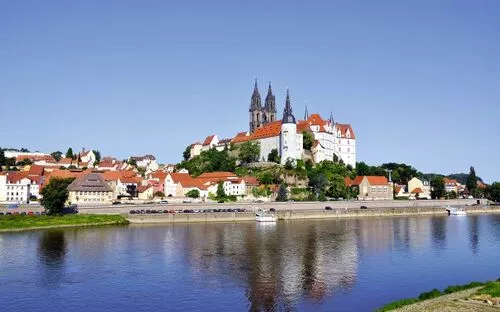 Stadtpanorama mit Schloss und Dom am Flussufer unter blauem Himmel.
