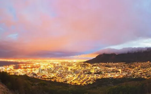 Luftaufnahme einer Stadt bei Dämmerung mit buntem Himmel und Bergen im Hintergrund.