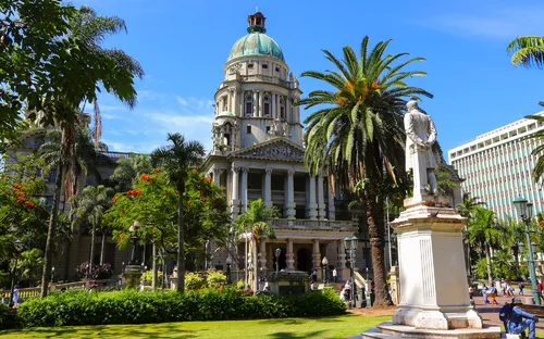 Das Bild zeigt das historische Rathaus von Durban in Südafrika, umgeben von Palmen und Statuen.