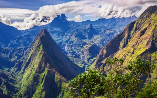 Blick auf bergige Landschaft mit üppigem Grün und dramatischen Gipfeln unter blauem Himmel.