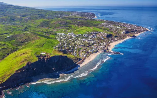 Luftaufnahme einer Küste mit grüner Landschaft und Dorf am Meer.