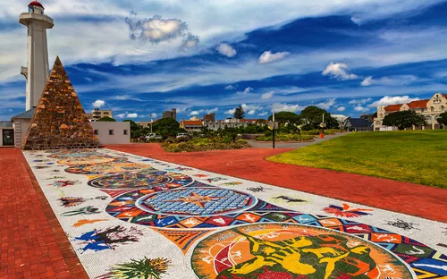 Bunt gestalteter Platz mit einem Leuchtturm und Pyramidenstruktur im Hintergrund.