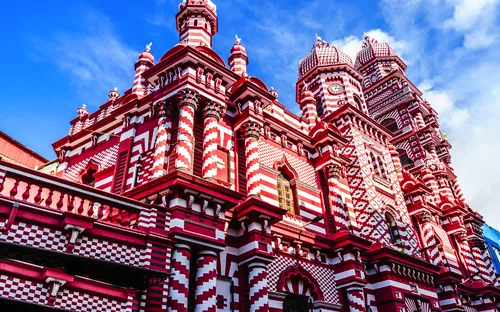 Rotes und weißes gemustertes Gebäude mit Türmen vor blauem Himmel.