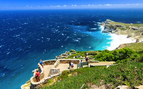 Menschen auf einem Aussichtspunkt mit Blick auf das Meer und eine felsige Küstenlandschaft.