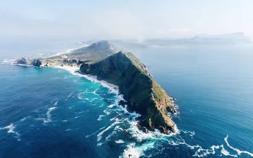 Luftaufnahme einer felsigen Küste mit tiefblauem Meer und Wellen.