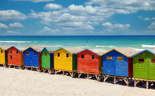 Bunte Strandhütten am Sandstrand mit blauem Himmel und Meer im Hintergrund.