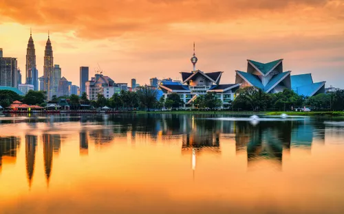 Stadtansicht von Kuala Lumpur bei Sonnenuntergang mit reflektierendem See.