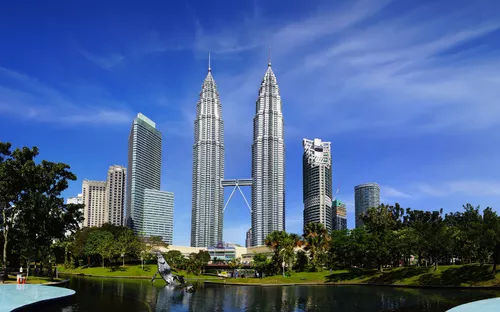 Die Petronas Towers in Kuala Lumpur hinter grünem Stadtpark und blauem Himmel.