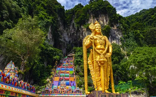Goldene Statue vor bunt bemalter Treppe und bewaldetem Felsen.