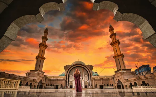 Frau steht vor Moschee bei Sonnenuntergang