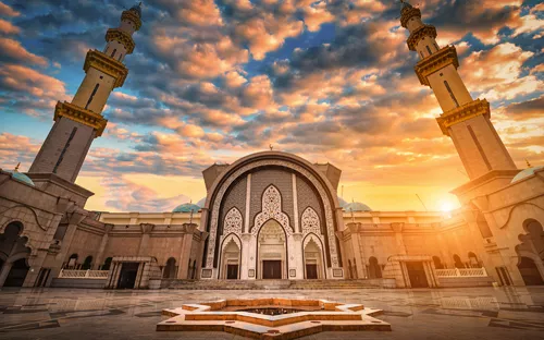 Moschee mit türkisfarbenen Kuppeln bei Sonnenuntergang, zwei Minarette im Vordergrund.