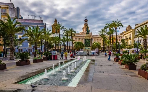Platz mit Springbrunnen und Palmen, umgeben von historischen Gebäuden.
