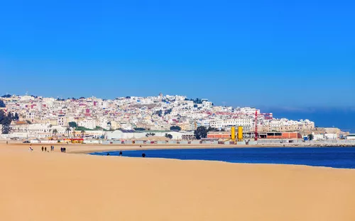 Stadtansicht von Tanger mit Sandstrand im Vordergrund unter blauem Himmel.