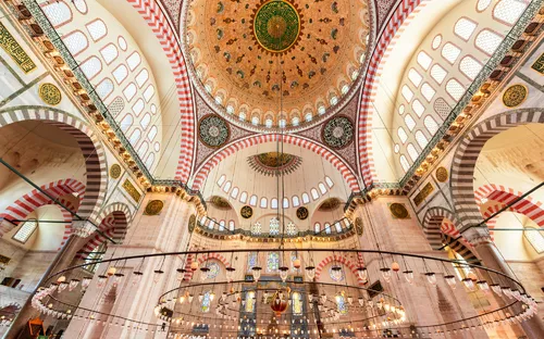 Innenansicht einer Moschee mit kunstvoller Decke und großen Bögen.