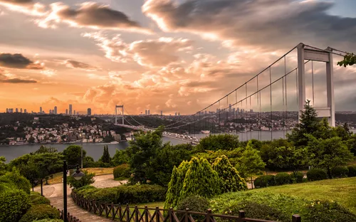 Brücke über Fluss mit Stadt und bewölktem Himmel im Hintergrund.