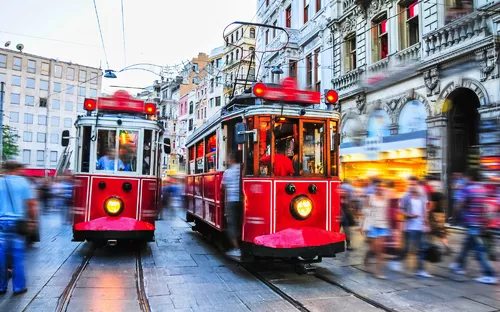 Zwei rote Straßenbahnen fahren durch eine belebte städtische Straße.