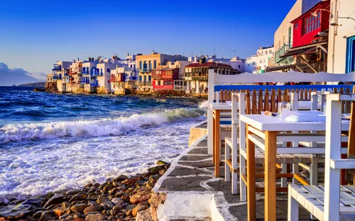 Tische am Meer vor der bunten Küste von Mykonos bei Sonnenuntergang.