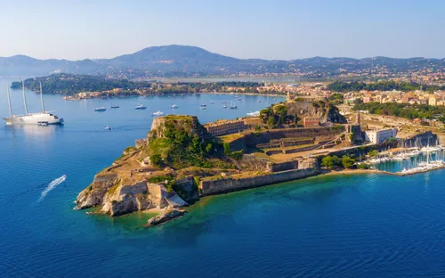 Luftaufnahme einer Insel mit alter Festung und Yachthafen im Mittelmeer.