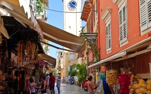 Schmale Gasse in Altstadt mit Geschäften und Kirchturm im Hintergrund bei sonnigem Wetter.