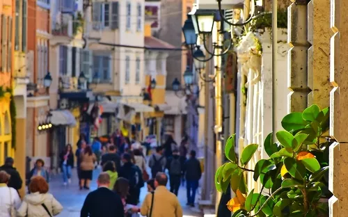 Blick auf eine belebte, sonnige Straßenszene mit Menschen und historischen Gebäuden.
