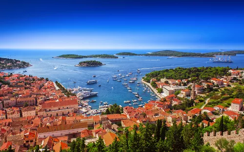 Küstenstadt mit Hafen und vielen Booten im Mittelmeerraum, umgeben von Inseln.