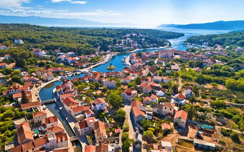 Luftaufnahme einer Küstenstadt mit Fluss, Häusern und bewaldeter Umgebung.