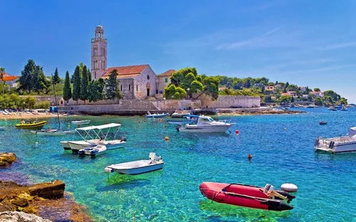 Boote auf türkisblauem Wasser mit einer historischen Kirche und üppiger Vegetation im Hintergrund.
