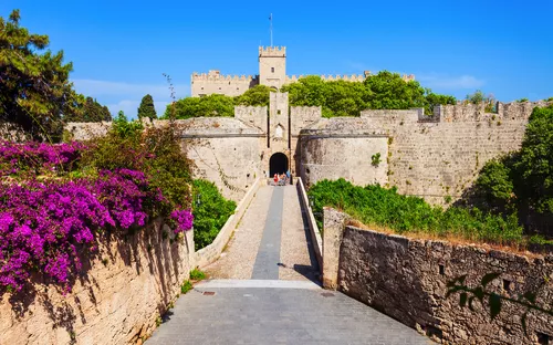 Mittelalterliche Burg mit Steinbrücke und blühenden Bougainvilleen.