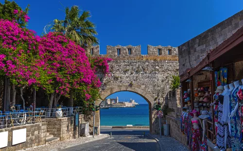 Stadttor mit Bougainvillea, Meerblick und Souvenirladen im Vordergrund.