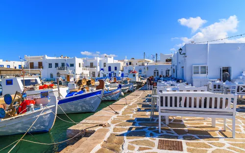 Hafen mit traditionellen weißen Gebäuden und Fischerbooten unter blauem Himmel.