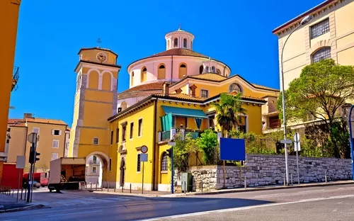 Gelbes Gebäude mit Kuppel und Glockenturm an einer Straßenecke bei klarem Himmel.