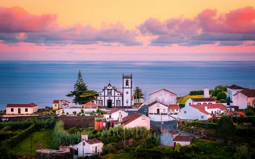 Küstenort mit Kirche bei Sonnenuntergang, im Hintergrund das Meer.