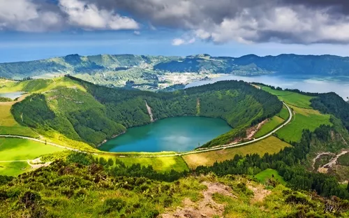 Grüner Vulkansee in hügeliger Landschaft mit bewölktem Himmel.