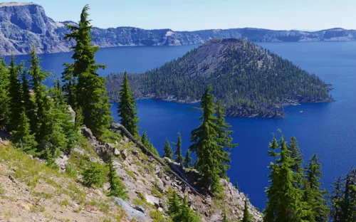 See mit bewaldeter Insel und umliegenden Bergen im Hintergrund.